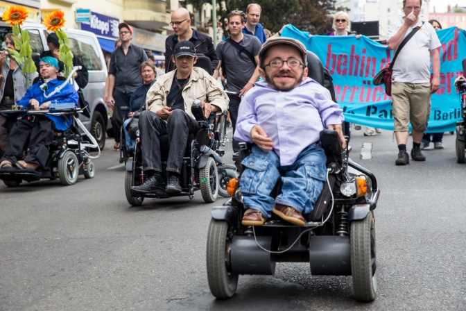 Verschiedene Menschen mit Behinderung mit Transparenten bei einer Parade