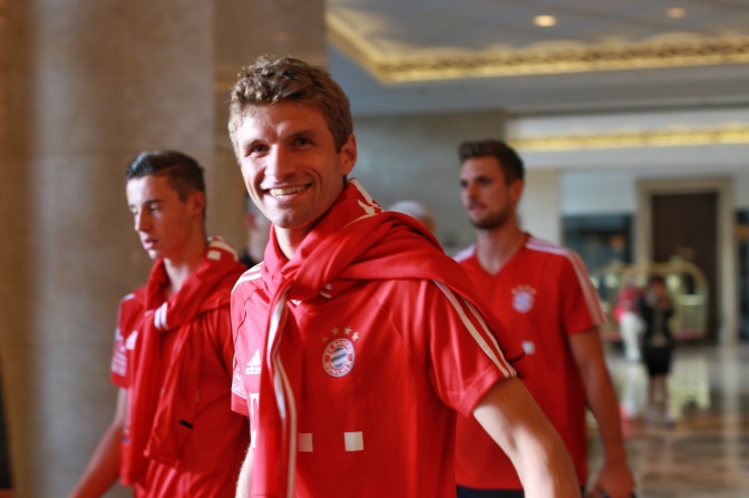 Thomas Müller in einem roten Bayern-München-Trikot, hinter ihm zwei Teamkollegen.