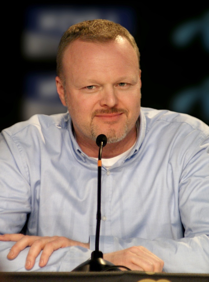 Stefan Raab mit Vollbart in einem hellblauen Hemd. Er sitzt vor einem Mikrofon.