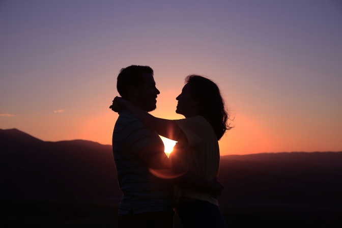 Ein Paar bei Sonnenuntergang. Man sieht nur die Silhouetten der beiden Personen.