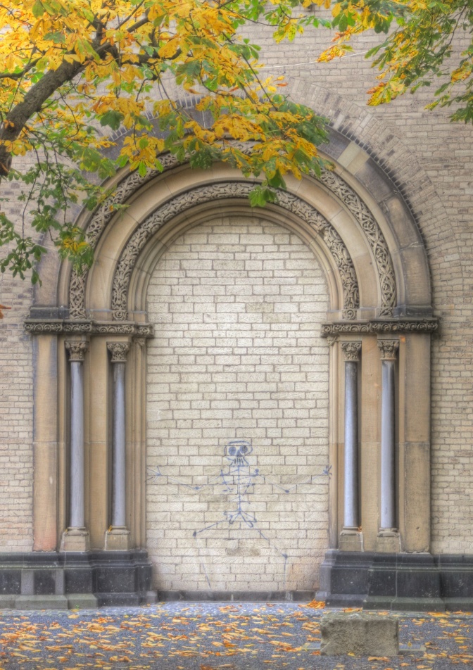 Ein in schwarzen Linien gespraytes Skelett an einer Wand unter einem Rundbogen.