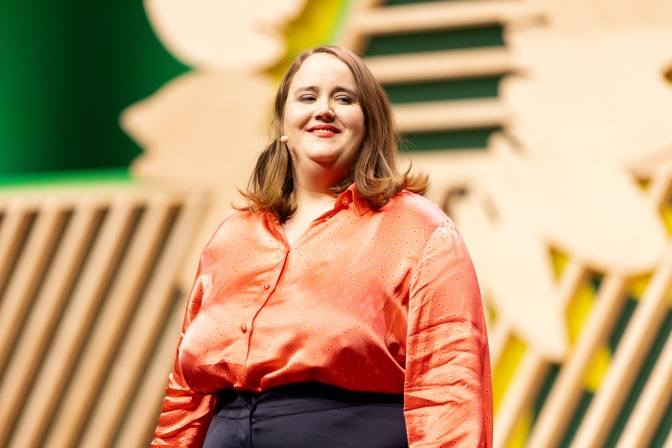 Ricarda Lang in einer pfirsichfarbenen Bluse. Sie steht locker und lächelt direkt in die Kamera.