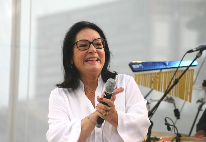 Nana Mouskouri in weißer Bluse mit einem Mikrofon in der Hand.