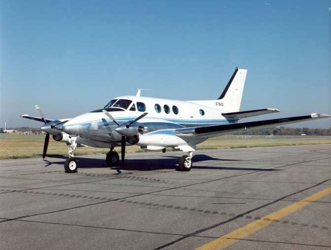 Ein kleines, weißes Flugzeug mit mehreren Propellern steht auf einem Rollfeld.