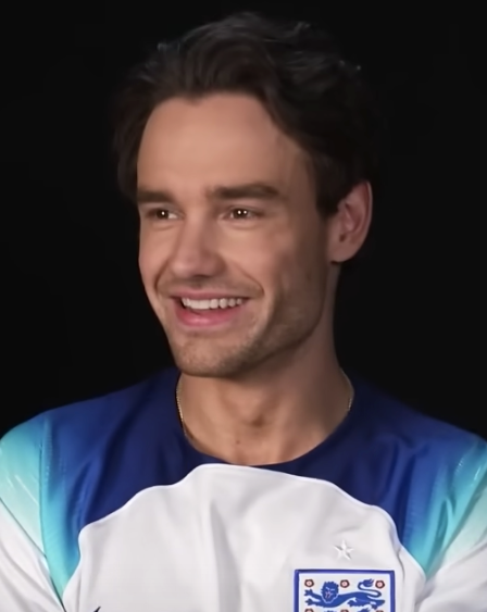 Liam Payne in einem blau-weißen Shirt mit kurze braune Haaren. Er lächelt breit.