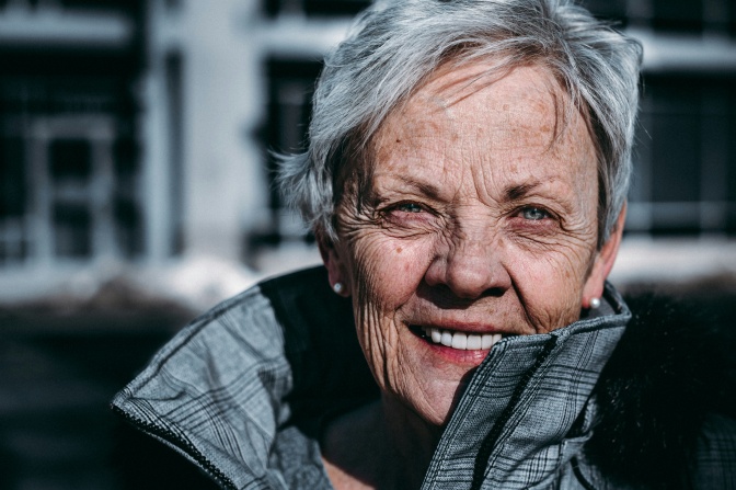 Eine alte Frau mit kurzen weißen Haaren schaut lächelnd direkt in die Kamera.