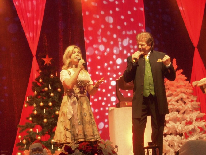 Marianne und Michael singen auf einer weihnachtlich dekorierten Bühne. Beide tragen Tracht.