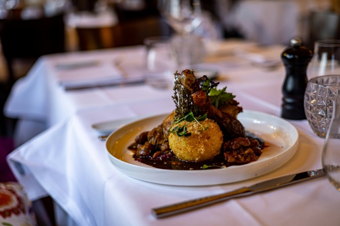 Ein Teller mit Essen an einem festlich gedeckten Tisch. Auf dem Teller leigt ein Knödel auf Soße und Gemüse.