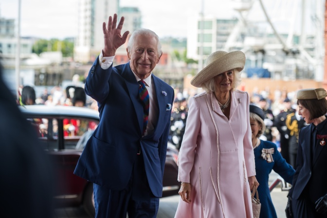 König Charles und seine Frau Camilla gehen durch eine Menschenmasse und winken den Menschen um sie herum zu.