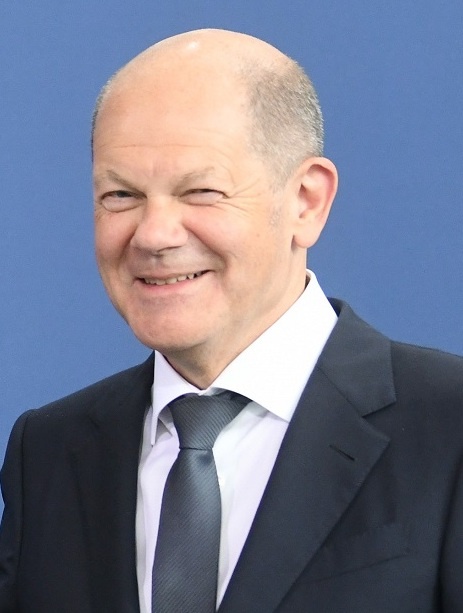 Olaf Scholz mit Stirnglatze in Anzug und Krawatte. Er lächelt breit.