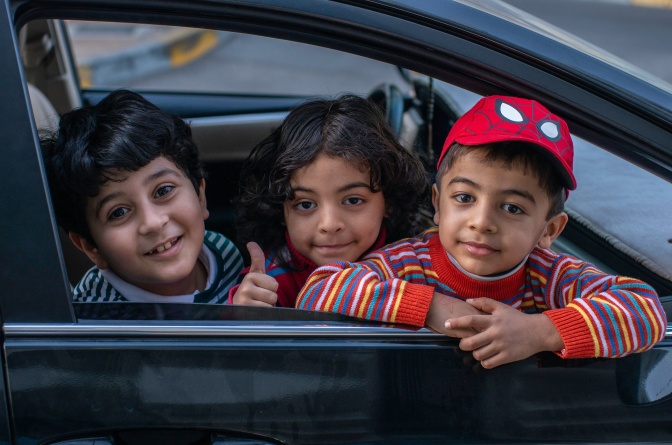 Drei Kinder sitzen nebeneinander im Auto, zwei Jungen und ein Mädchen.