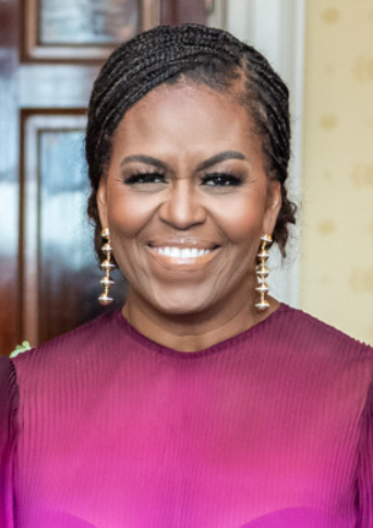 Michelle Obama mit Braids. Sie lächelt breit in die Kamera und trägt ein pinkfarbenes Kleid und lange goldene Ohrringe.