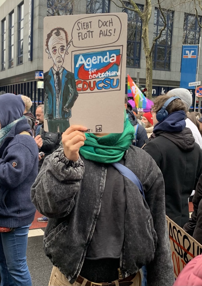 Jemand hält ein selbstgeschriebenes Demo-Schild vor das eigene Gesicht. Darauf sieht man den Schriftzug der CDU im Design der AfD.