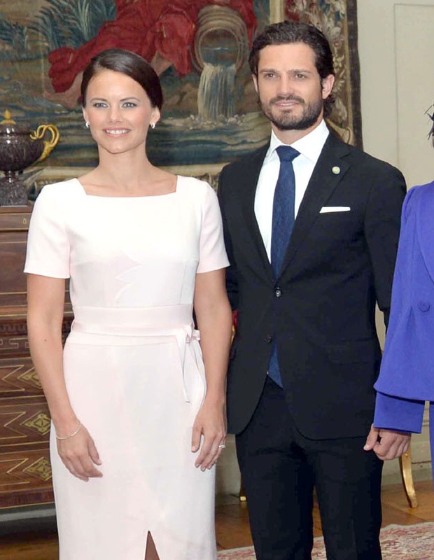 Carl Philip und Sofia von Schweden stehen in festlicher Kleidung nebeneinander und lächeln in die Kamera.