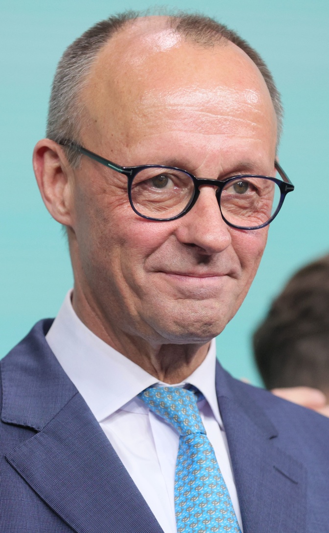 Friedrich Merz in Anzug und Krawatte. Er trägt Brille und lächelt.