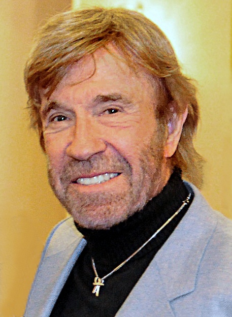 Chuck Norris  mit Vollbart, in Sakko und Rollkragenpullover. Er lächelt in die Kamera.