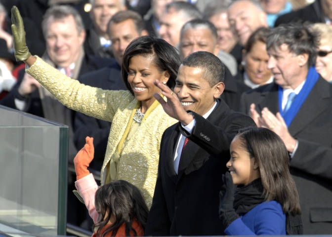 Michelle und Barack Obama in einer großen Menschenmenge. Sie lächeln und winken.