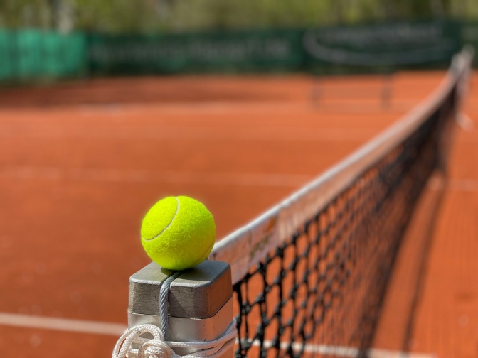 Ein Tennisball liegt auf der Stange, die das Tennisnetz hält.