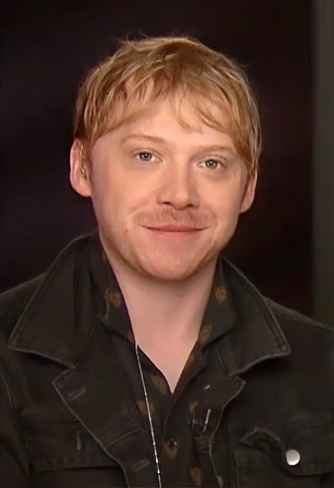 Rupert Grint mit Dreitagebart und roten Haaren. Er trägt Schatz und schaut direkt in die Kamera.