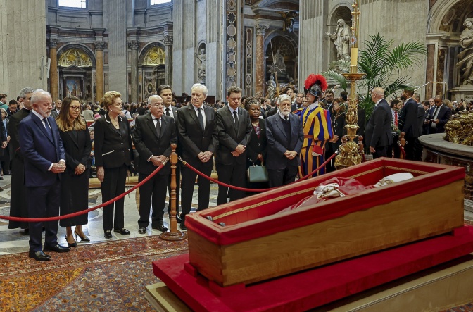 Der Papst liegt aufgebahrt in einem rot ausgekleideten Sarg. Um ihn herum stehen Trauergäste in Schwarz.