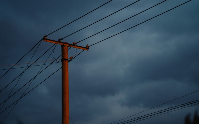 Oberirdische Stromleitungen an einem Mast vor dunklem, bewölktem Himmel