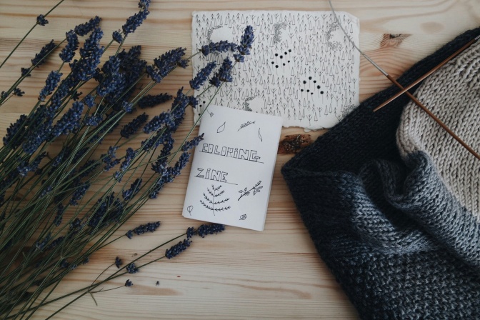 Ein Zine mit Zeichnungen in schwarz-weiß liegt neben einem Strickzeug und Lavendelzweigen.