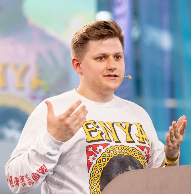 Sebastian Hotz in einem weißen Sweatshirt mit Print. Er spricht und gestikuliert mit den Händen.
