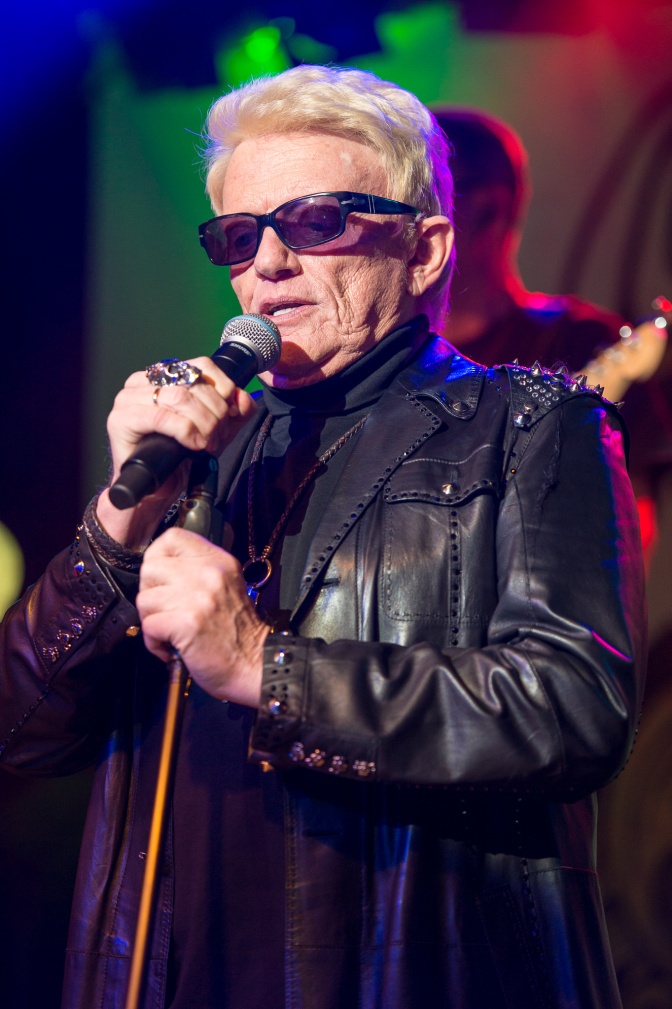Heino mit Sonnenbrille in schwarzer Lederkleidung auf der Bühne. Er singt in ein Mikro.