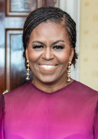 Michelle Obama lächelt direkt in die Kamera. Sie trägt ein pinkfarbenes Kleid und hängende Ohrringe. Ihre Haare sind zu Braids geflochten.