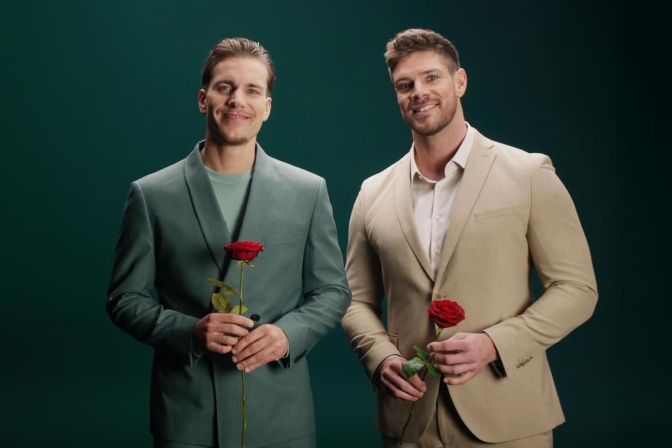 Zwei Männer stehen nebeneinander. Beide tragen Anzug und halten eine Rose in der Hand.