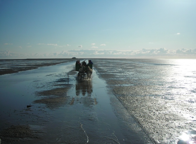 Eine Pferdekutsche fährt über einen Wall, rechts und links Meer.