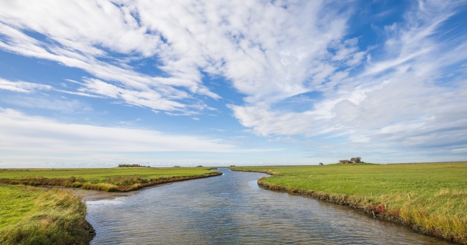 Ein bewölkter Himmel über einer flachen Wiese, Teile davon sind überflutet.