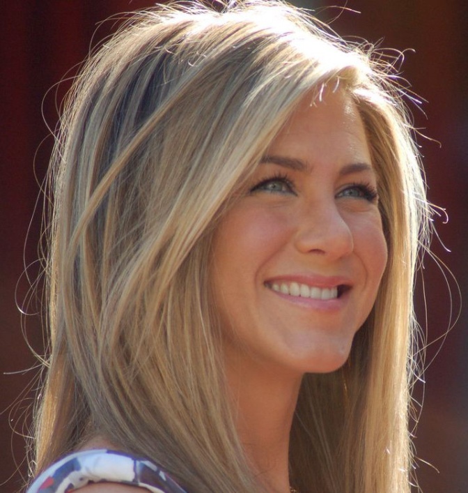 Jennifer Aniston mit glatten schulterlangen Haaren. Sie lächelt und schaut an der Kamera vorbei ins Weite.