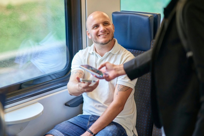 Ein Mann sitzt im Zug. Er zeigt sein Handyticket bei einer Kontrolle vor.