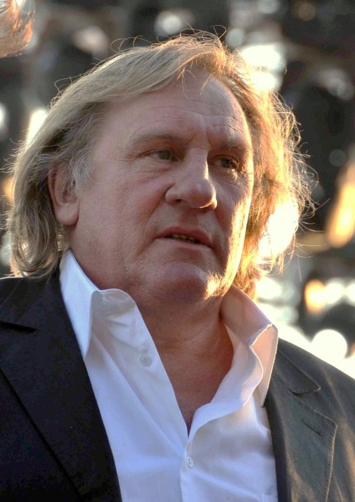 Gérard Depardieu mit kinnlangen blonden Haaren in weißem Hemd und Sakko