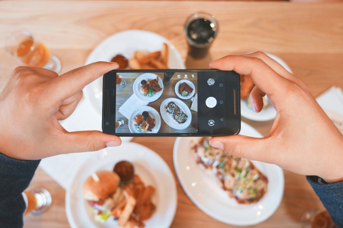 Jemand fotografiert Essen auf 4 Tellern mit dem Handy.