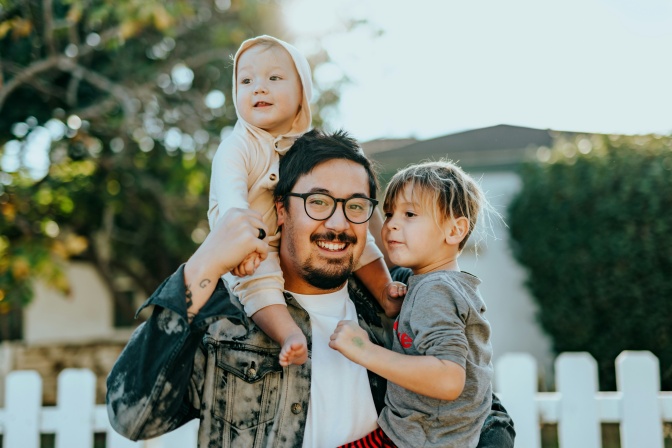 Ein asiatischer Mann mit 2 Kindern. Das jüngere Kind sitzt auf seinen Schultern.