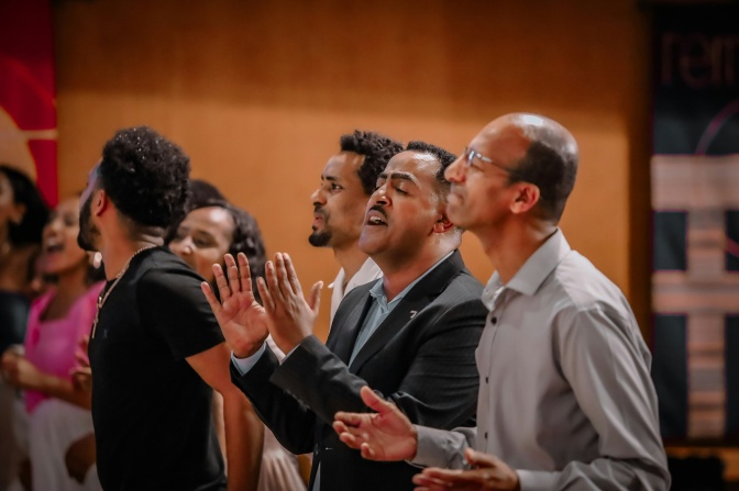 Mehrere POC Personen stehen nebeneinander und singen.