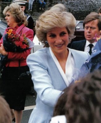 Prinzessin Diana in einem hellblauen Kostüm. Sie schüttelt lächelnd Menschen die Hand.