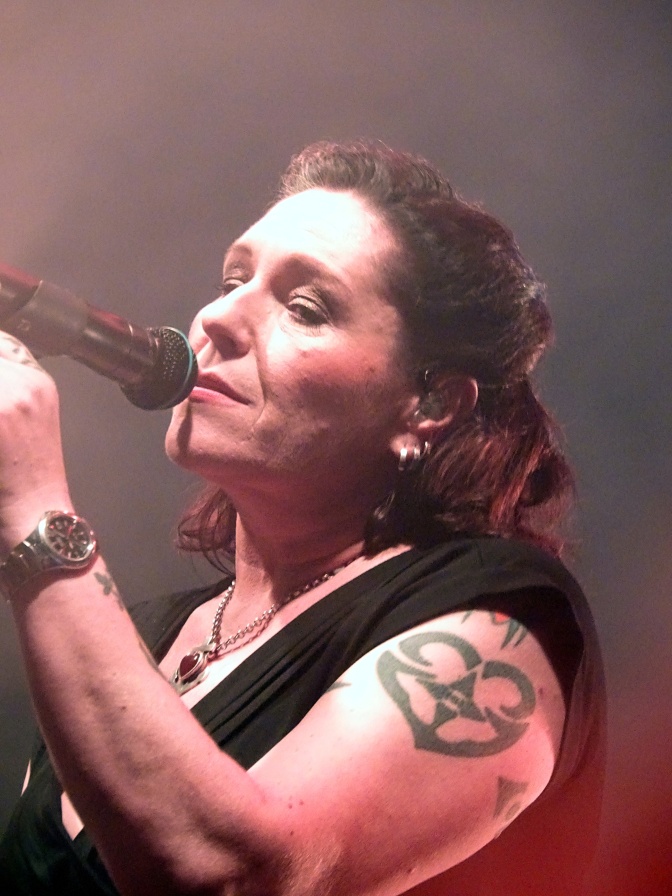 AnNa R. singt in ein Mikro. Sie trägt schwarz und hat ein großes Tattoo auf Oberarm und Schulter.