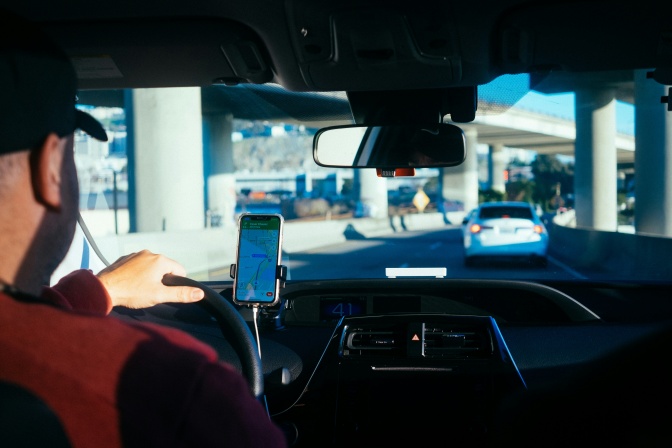 Eine Person fährt ein Auto durch den Stadtverkehr und hat die Navigation am Handy geöffnet.