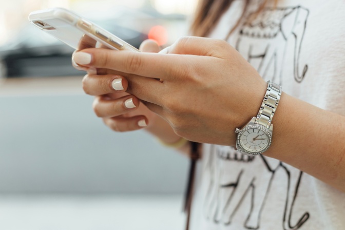 Eine Frau hält ein Handy in beiden Händen. Man sieht nur Hände und Gerät im Bildausschnitt.