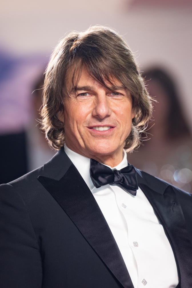 Tom Cruise mit etwas längeren braunen Haaren. Er lächelt in die Kamera und trägt Anzug und Fliege.