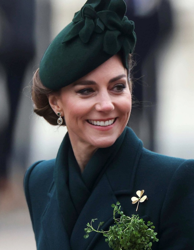 Prinzessin Kate in einem dunkelgrünen Mantel mit schräg sitzendem passenden Hut. Sie lächelt und schaut seitlich an der Kamera vorbei.