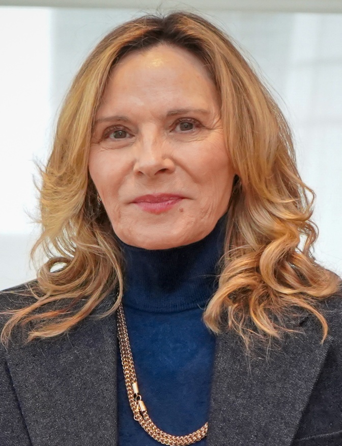 Kim Cattrall mit schulterlangen rotblonden Haaren in einem schwarzen Rolli mit Sakko. Sie lächelt leicht.