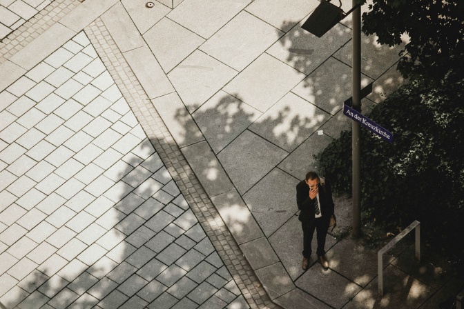 Ein Mann in Anzug steht im Schatten und raucht eine Zigarette.