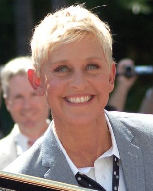 Ellen deGeneres mit kurzen blondierten Haaren in einem Anzug und Hemd.