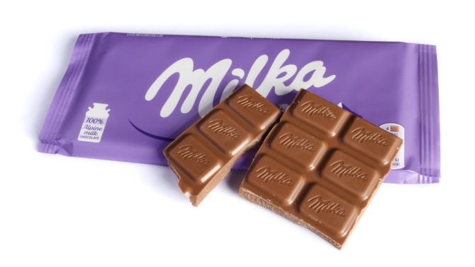 Eine Tafel Schokolade, von der einige Riegel abgebrochen sind, liegt auf einer lilafarbenen Verpackung von Milka