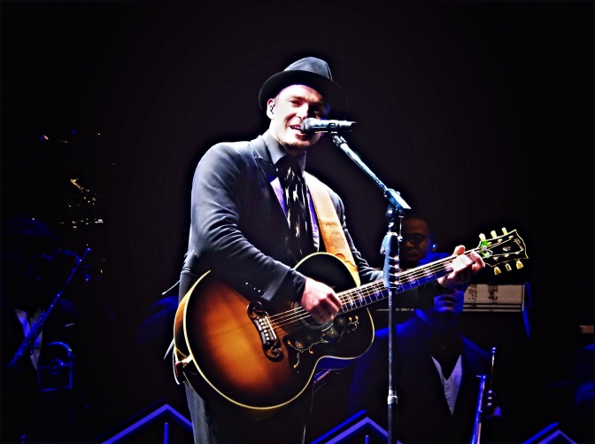 Justin Timberlake mit Hut und akustischer Gitarre auf der Bühne.