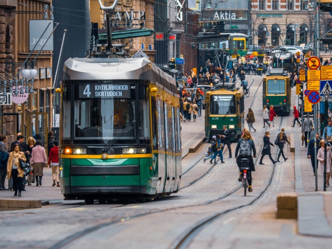 Zwei Straßenbahnen, Fußgänger*innen und Fahrradfahrer*innen auf einer Straße in Helsinki